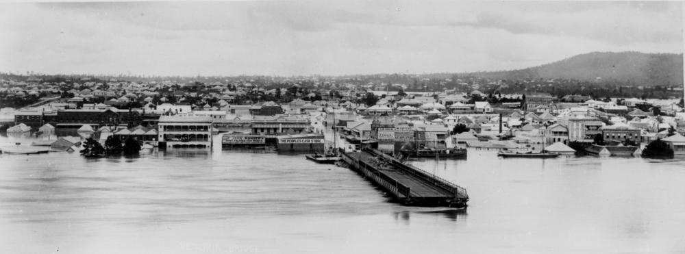 View of South Brisbane during the 1893 floods. Photograph shows the first permanent Victoria Bridge, half demolished by the flood. A number of buildings along the river are almost completely submerged under the floodwaters.   'John Oxley Library, State Library of Queensland   Image: 91660'.